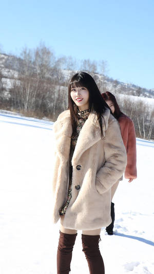 穿米色外套的女子在雪地中微笑，背景有光禿樹木和山丘。 — 平井もも 壁紙