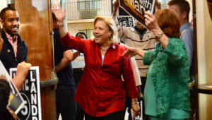 政治家在室內向舉著競選標語牌歡呼的支持者揮手。 — 美國 壁紙