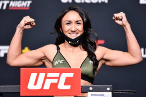 女性UFC拳手在稱重活動中展示肌肉，穿著綠色運動胸罩和黑色口罩。 — 酷 壁紙
