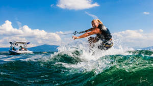 女性在波濤洶湧的藍色水面上滑水，身後有一艘快艇。 — 衝浪 壁紙