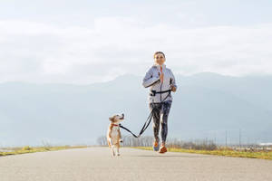 女性在陰天時在山附近用皮帶牽狗慢跑 — Running 壁紙