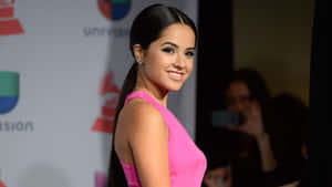 身穿粉色連衣裙的女性在紅地毯活動中微笑，背景有Univision和Grammy標誌。 — 貝琪·G 壁紙