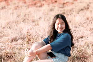 年輕女性微笑著坐在草地上手持野花。 — 海軍藍 壁紙