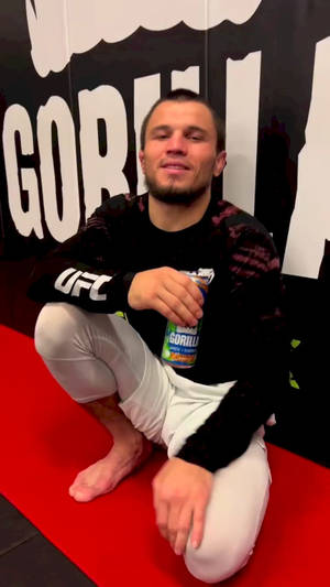 一位UFC戰士蹲在紅色墊子上手持能量飲料。 — 終極格鬥冠軍賽 壁紙