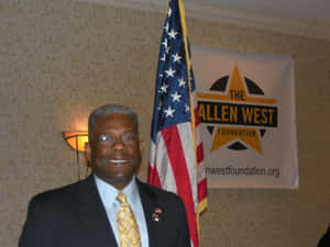 活動中穿著西裝的男士微笑，背後有美國國旗和Allen West Foundation橫幅。 — 政治 壁紙