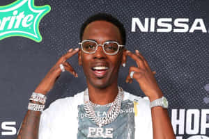 戴眼鏡和珠寶的男子在活動中於品牌背景前擺姿勢。 — Young Dolph 壁紙