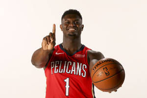 身穿紅色Pelicans球衣的籃球運動員手持籃球並向上指。 — 錫安·威廉森 壁紙