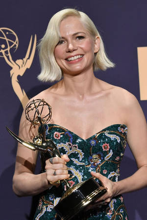身穿花卉裙的女子在活動中手持艾美獎獎座 — 女演員 壁紙