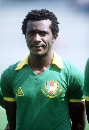 身穿綠色和黃色Lions Indomptables球衣的黑人足球員對著鏡頭微笑。 — FIFA 世界盃 壁紙