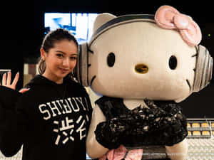 黑帽T女性在戴著耳機和蕾絲服裝的巨型Hello Kitty吉祥物旁邊揮手。 — 東京喰種風格 壁紙