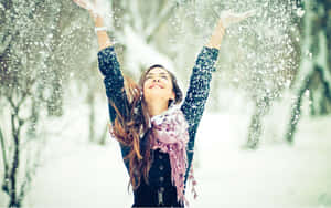 穿著冬季外套和圍巾的女性在戶外高舉雙臂拋雪。 — 冬季美學 壁紙