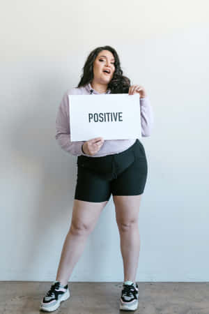 一位開心的女性在室內舉著寫有「positive」的標語牌。 — 模特兒 壁紙