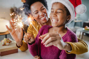 一位母親和女兒在室內節日慶祝活動中微笑著拿著煙花棒。 — 新年快樂 2020 壁紙