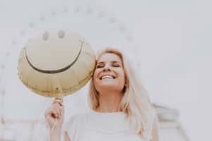 一位微笑的女性在戶外手持金色笑臉氣球。 — 正向 壁紙