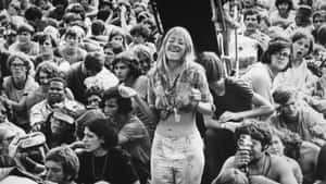 一位微笑的女士在1970年代的戶外音樂會上，被人群包圍著跳舞。 — Woodstock 壁紙