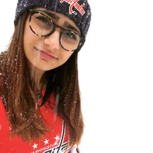 穿著冬季服裝的年輕女性，頭髮和衣服上沾著雪花微笑。 — 米婭·哈利法 壁紙