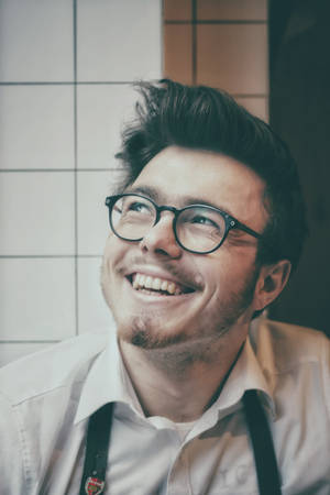 一位戴眼鏡和鬍子的微笑男子在瓷磚房間裡。 — 好運 壁紙