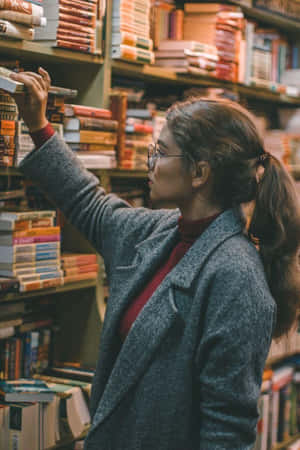 女性在舒適的書店中瀏覽書籍，燈光溫暖。 — 博物館 壁紙