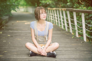 戴眼鏡的年輕女性盤腿坐在公園的木製步道上。 — 日本 壁紙