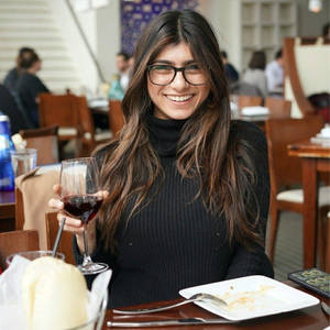 女性在餐廳桌上拿著一杯紅酒微笑。 — 米婭·哈利法 壁紙