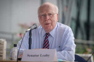 參議員 Leahy 在正式會議中發言，配有麥克風和名牌。 — 低調 壁紙