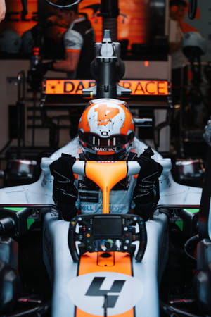 戴著橙色和白色頭盔的F1車手在賽車內，帶有贊助商標誌。 — F1 iPhone 壁紙