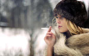 穿著毛大衣和帽子的女性在雪白的冬日場景中抽煙。 — 雪 壁紙