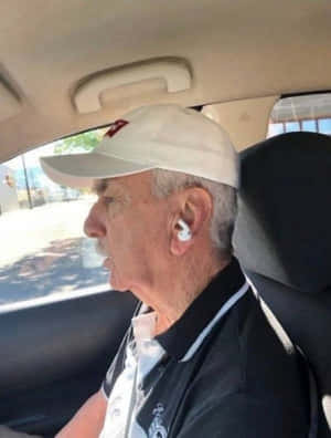 一位留鬍鬚、戴著帽子和耳塞的年長男性坐在汽車裡。 — 老人 壁紙