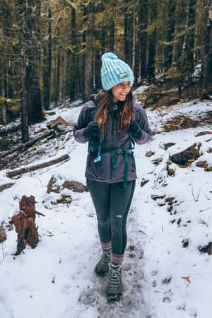 女性在雪地森林中徒步，戴著青綠色帽子和冬季裝備 — 冬季風景 壁紙