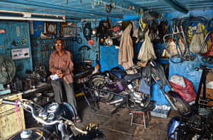 一位技師在雜亂的藍色機車維修店工作，店內充滿工具和機車。 — 巴布風機車 壁紙