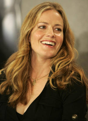 一位微笑的金髮女性，穿著黑色外套，戴著金色項鍊。 — 女演員 壁紙
