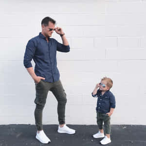 父親和幼兒穿著相配的服裝和太陽眼鏡，站在白色磚牆前。 — 情侶擁抱 壁紙
