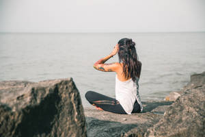 有刺青的女性坐在岩石上，面向日落時分的海洋。 — 海洋 壁紙