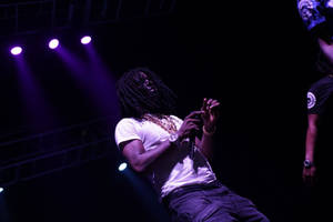 說唱歌手在紫色燈光下，帶著辮子和金鏈在舞台上表演。 — Chief Keef 壁紙