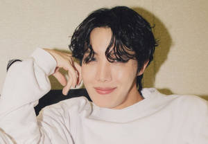 深色頭髮的年輕男子，身穿白色衛衣，將手放在臉旁微笑。 — Bts 壁紙