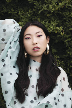 身穿圓點襯衫和金色耳環的年輕女性在戶外綠色背景下擺姿勢。 — 美學白 壁紙