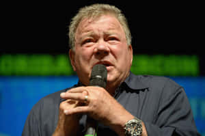 男子在綠色和藍色背景的活動中對著麥克風發言。 — 派大星 GIF 壁紙