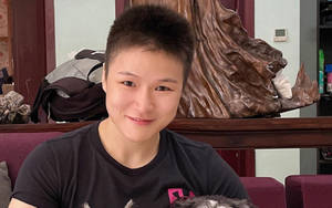 一位留著短髮的年輕人，在室內靠近一個木雕坐著微笑。 — 運動 壁紙