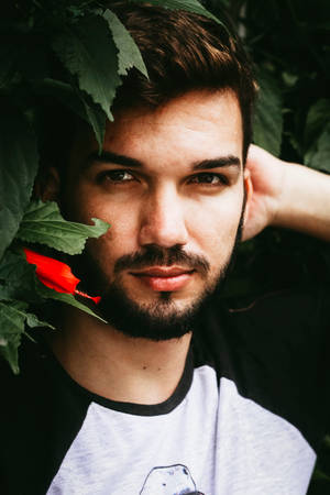 一位穿黑白襯衫的鬍鬚男子，被綠葉和紅花環繞。 — 模特兒 壁紙