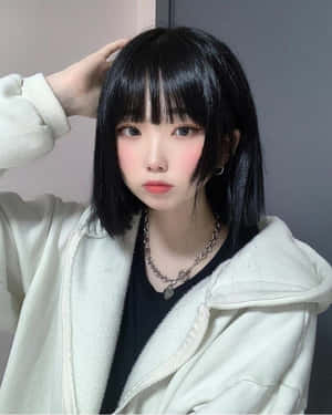留著黑色鮑伯頭的年輕女性，在室內穿著奶油色連帽衫和銀色鏈條項鍊。 — 垃圾美學 壁紙