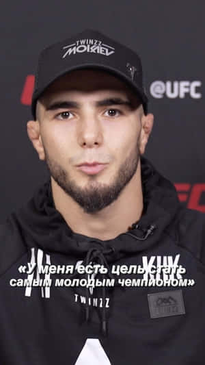 年輕男性運動員在UFC活動中戴黑色鴨舌帽和連帽衫，帶有俄語引文疊加。 — 運動 壁紙