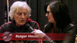Rutger Hauer 正接受一位戴眼鏡、手持麥克風的女子訪問。 — 演員 壁紙