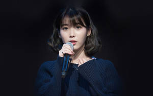 年輕女性手持麥克風穿著深藍色毛衣（黑色背景） — K Pop 壁紙
