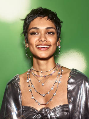 一位短髮的時尚女性在綠色背景下微笑，佩戴著多層寶石項鍊和圈形耳環。 — 珠寶 壁紙