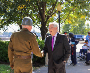 兩位長者在陽光明媚的日子裡在樹下戶外握手。 — 5:4 壁紙