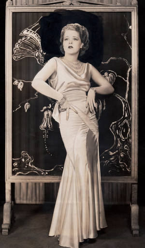 一位穿著1920年代絲綢長袍的女性在裝飾藝術風格屏風前擺姿勢的復古肖像。 — 克拉拉·鮑 壁紙