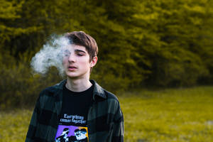 年輕男子在綠色森林中呼出煙霧。 — 吸大麻 壁紙