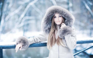 穿著帶毛帽的冬季外套的女子站在積雪的橋上。 — 冬季美學 壁紙