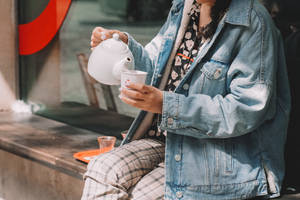 人將白色水壺中的茶倒入杯中，坐在戶外長椅上。 — 茶 壁紙