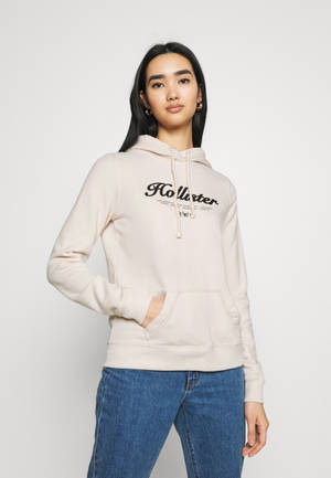 女性在工作室環境中穿著米色Hollister連帽衫和藍色牛仔褲。